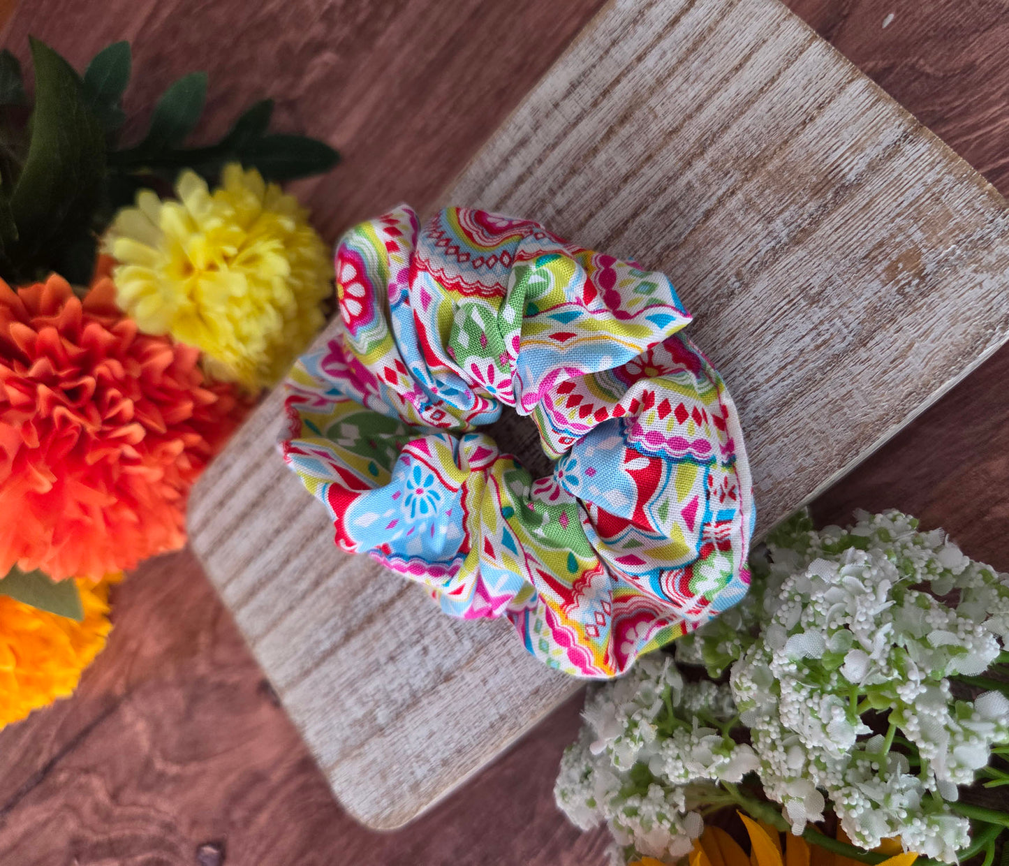 Colorful patterned scrunchie on a wooden surface with flowers in the background