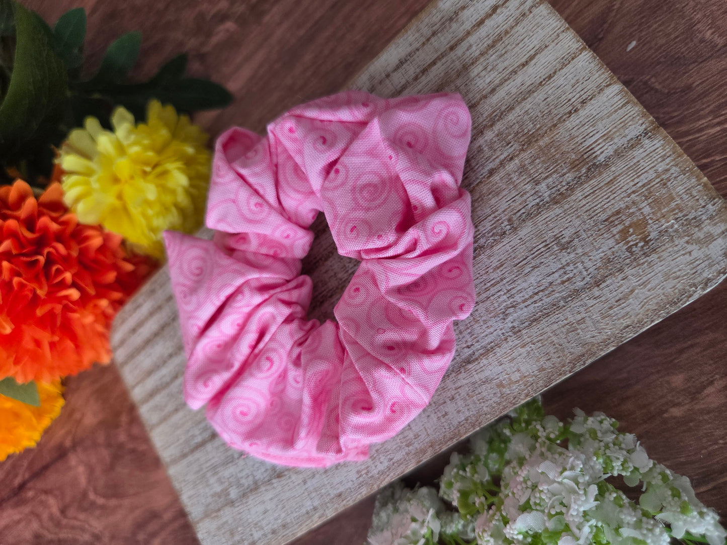 Pink textured scrunchie on a wooden surface with flowers in the background