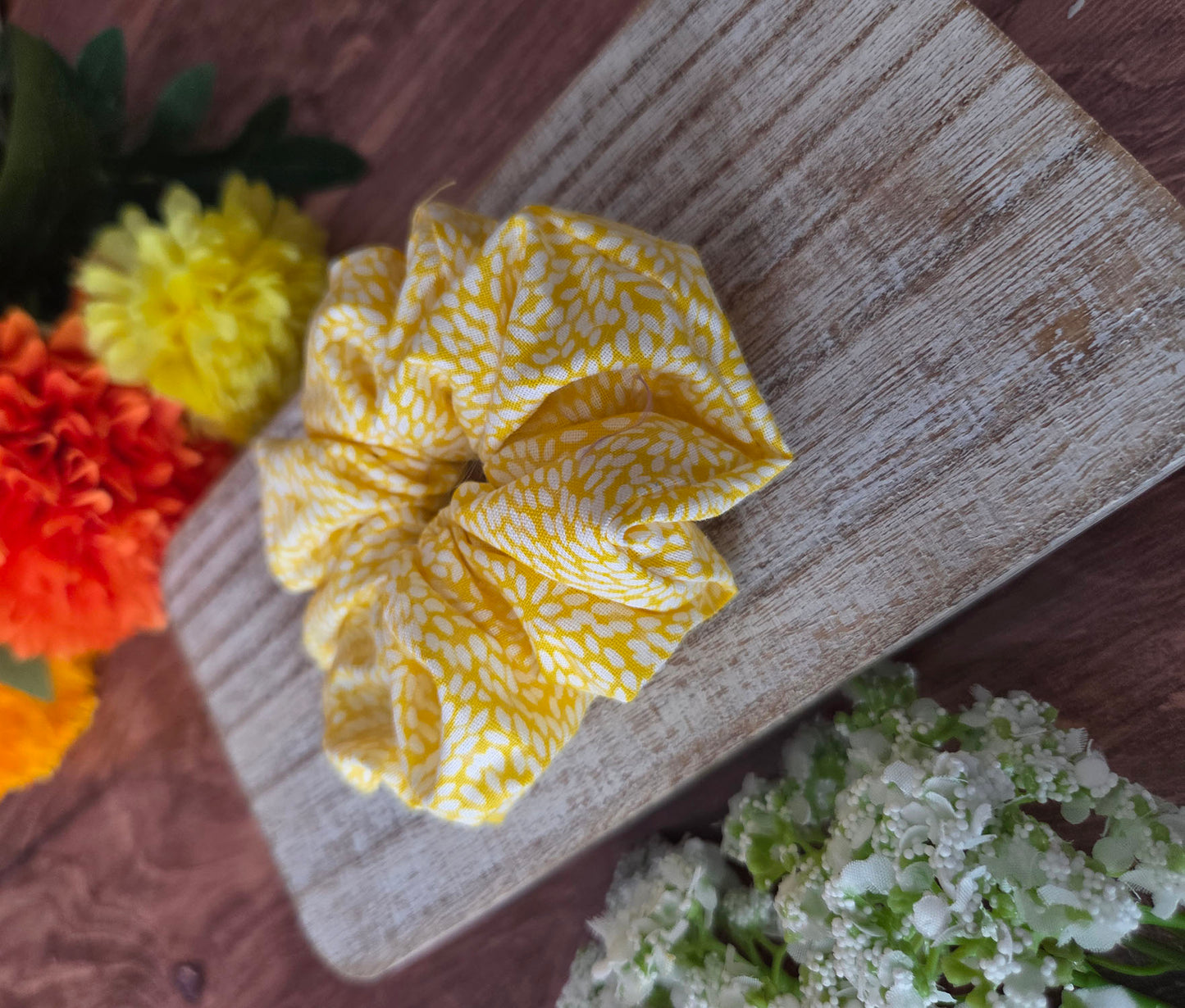 Yellow scrunchie on a wooden surface with flowers in the background