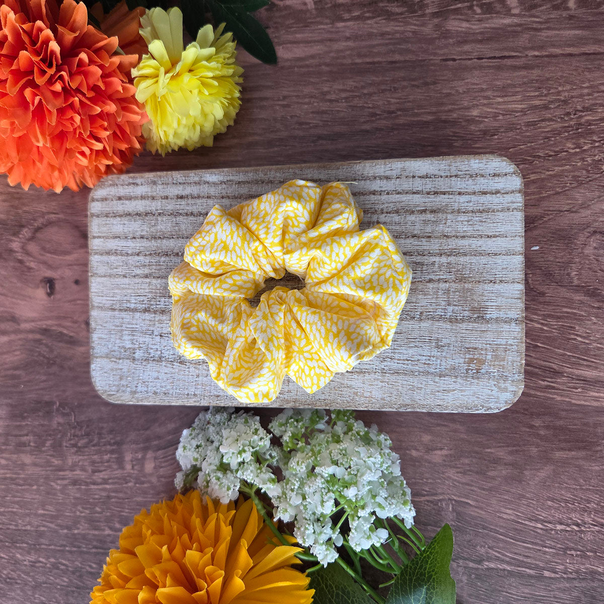 Yellow scrunchie on a wooden board with flowers around