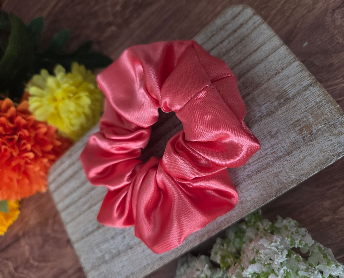 Pink satin scrunchie on a wooden surface with flowers in the background