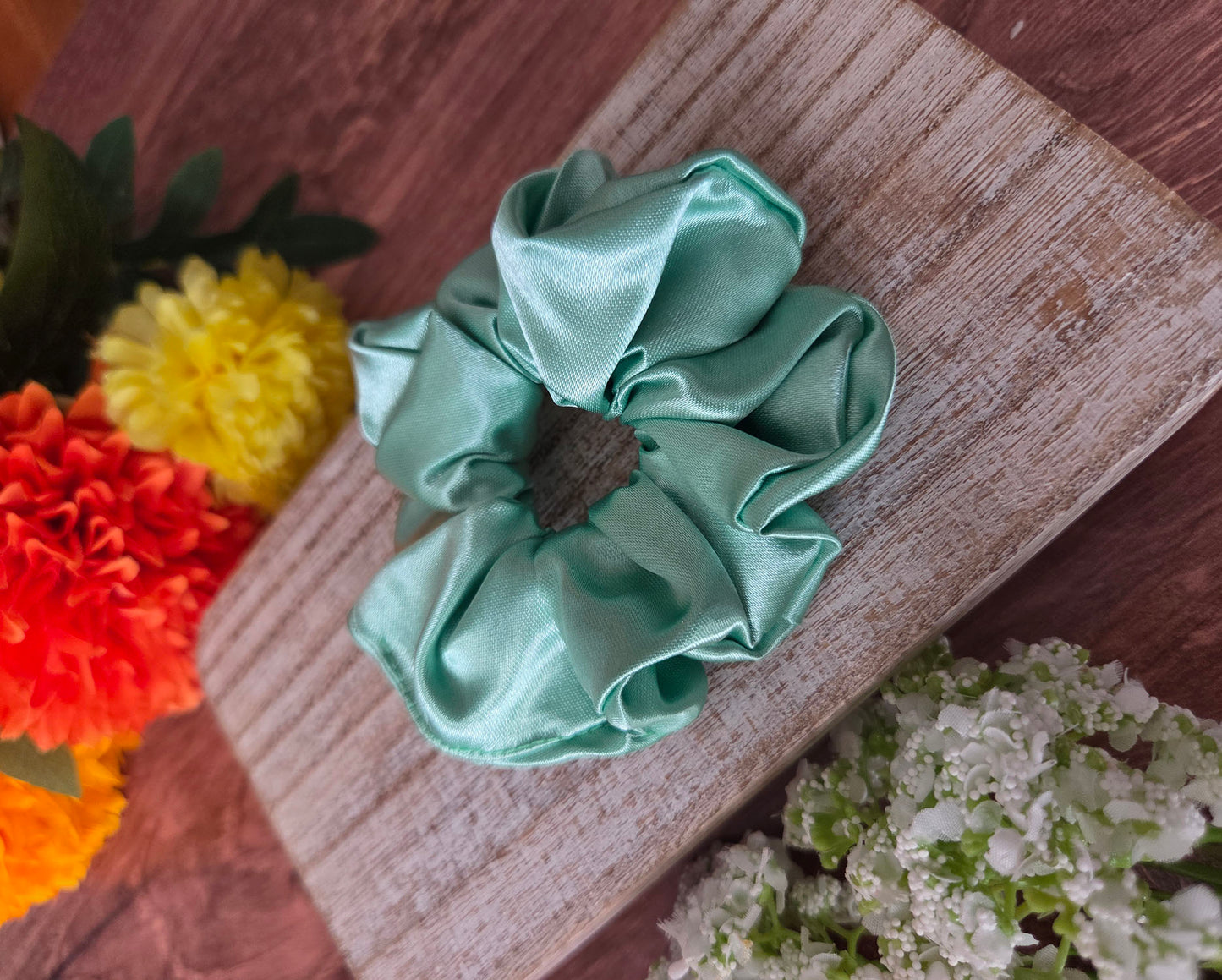 Green scrunchie on a wooden surface with flowers in the background