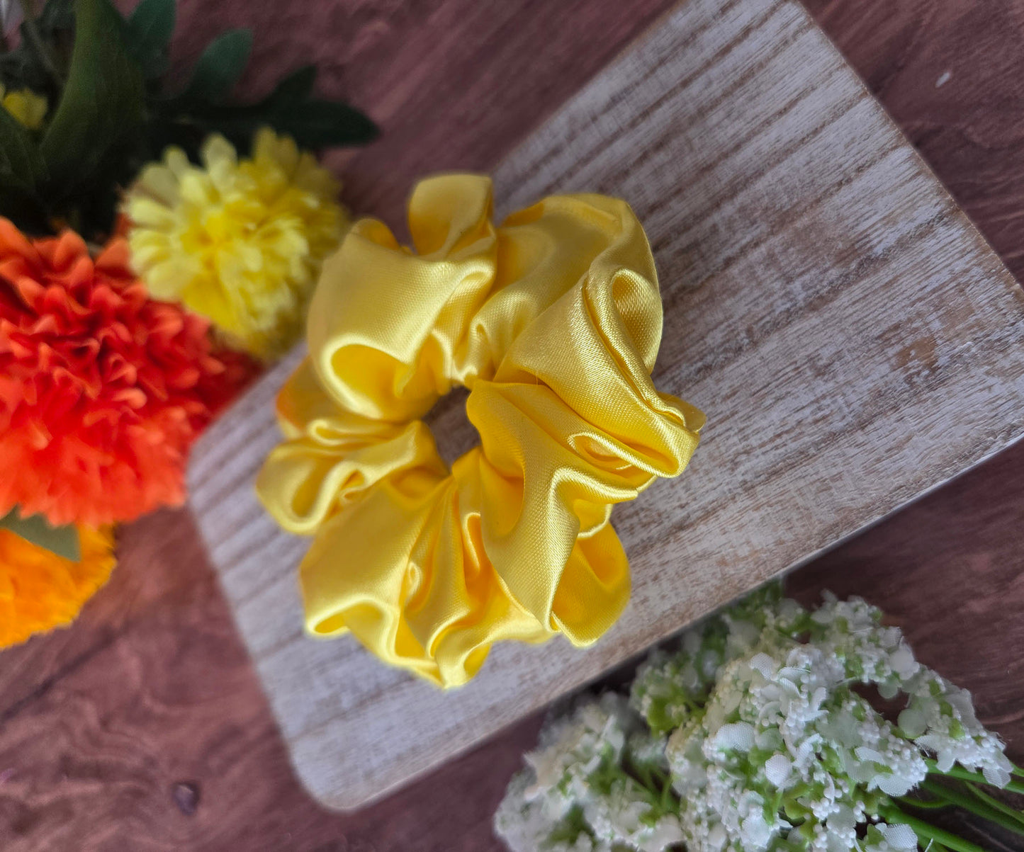 Yellow scrunchie on a wooden surface with flowers in the background