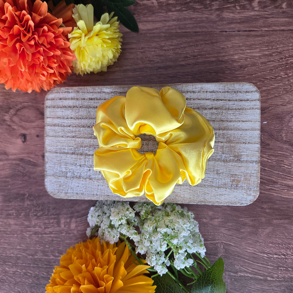 Yellow scrunchie on a wooden block with flowers around
