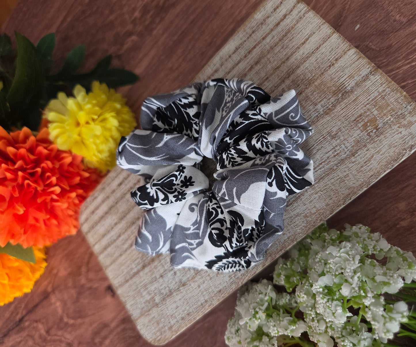 Black and white patterned scrunchies on a wooden board with flowers in the background