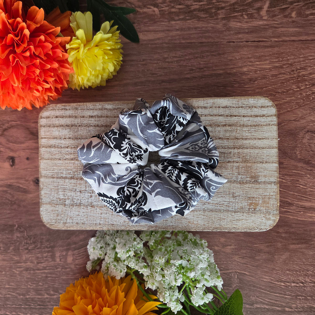 Black and white patterned scrunchie on a wooden board with flowers around