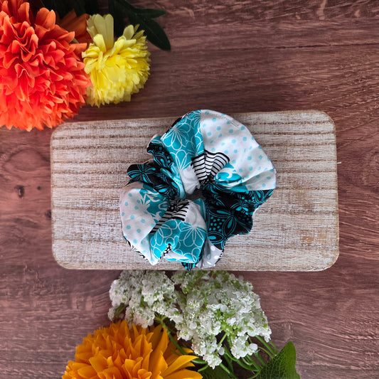 Three scrunchies on a wooden board with flowers around