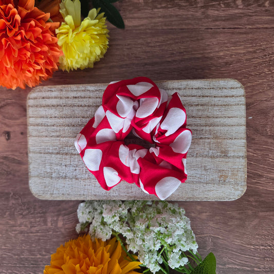 Red and white polka dot scrunchie on a wooden board with flowers around