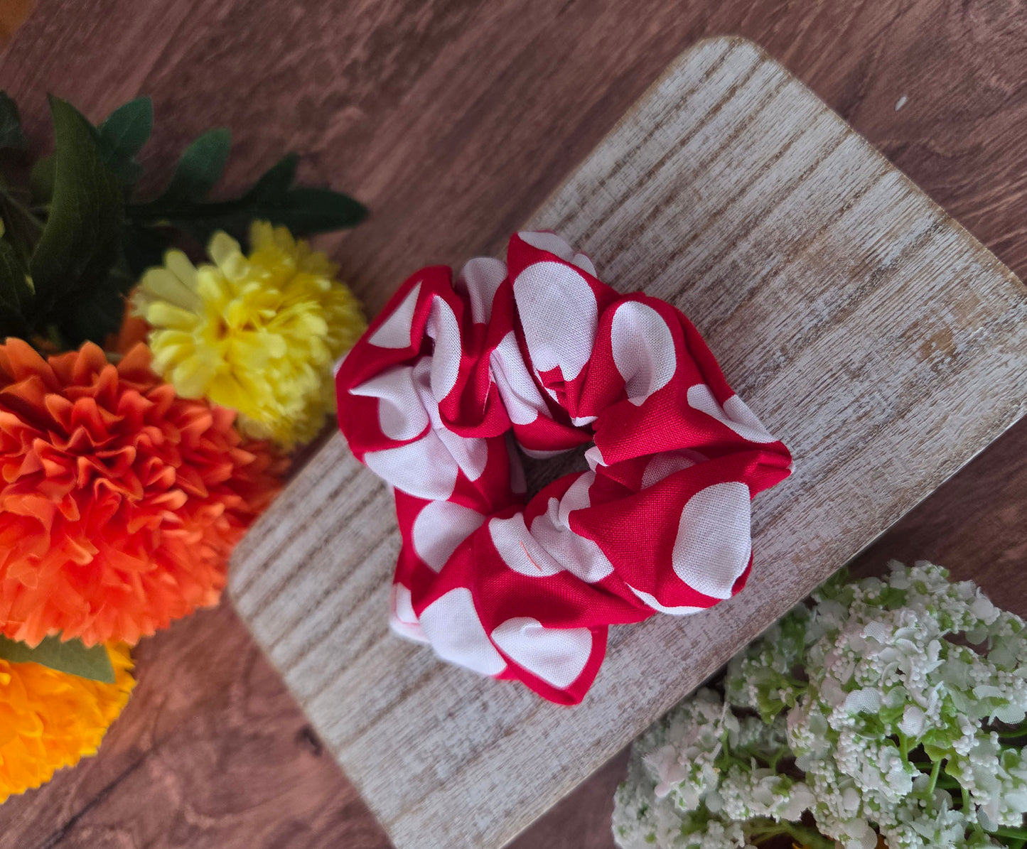 Red and white polka dot scrunchie on a wooden surface with flowers in the background