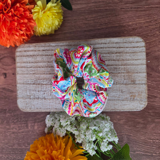 Colorful scrunchie on a wooden block with flowers around
