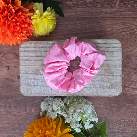 Pink scrunchie on a wooden board with flowers around