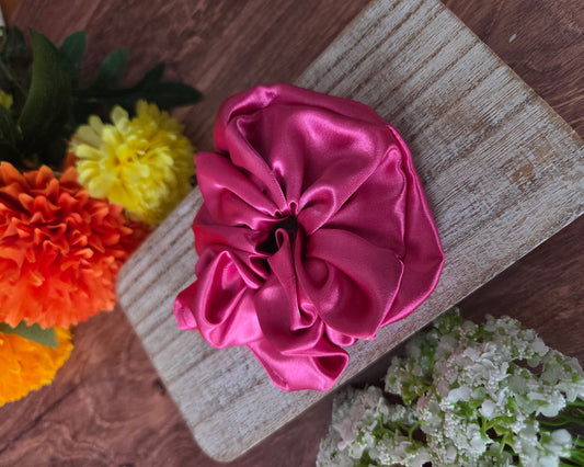 Pink satin flower on a wooden surface with flowers in the background