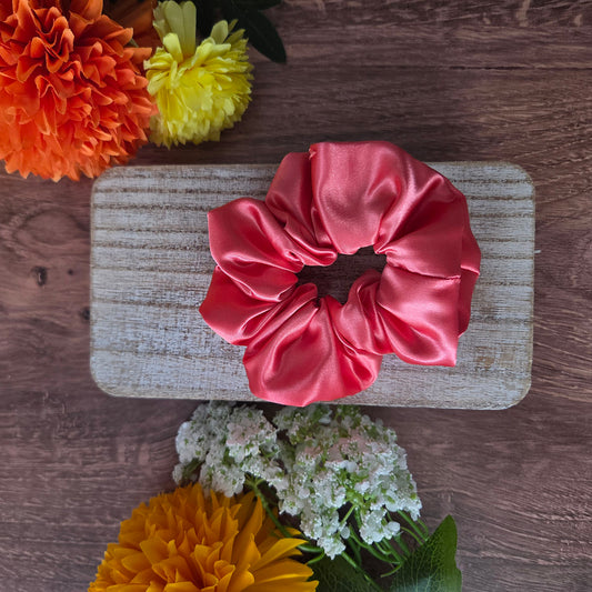Pink satin scrunchie on a wooden surface with flowers around