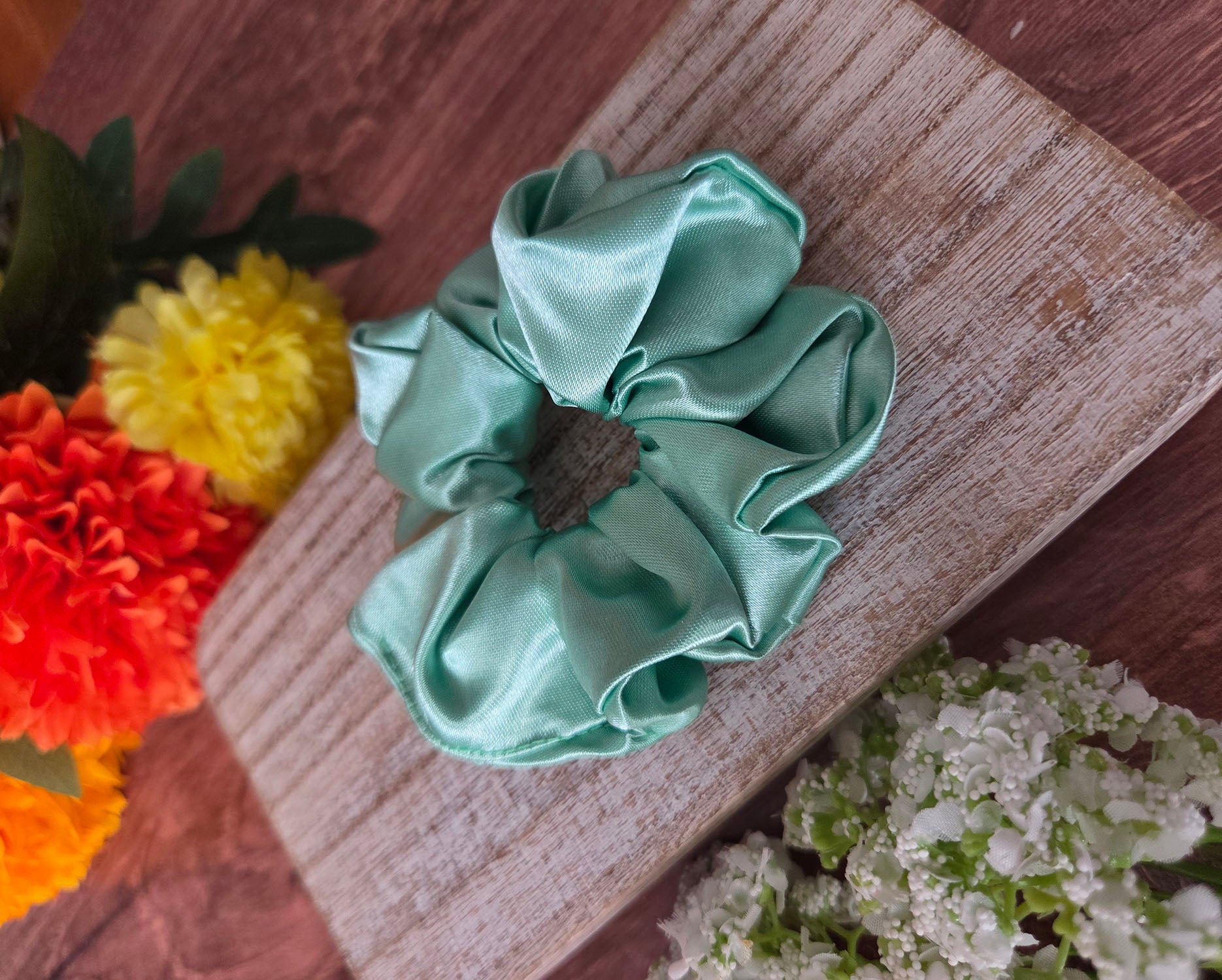 Green scrunchie on a wooden surface with flowers in the background