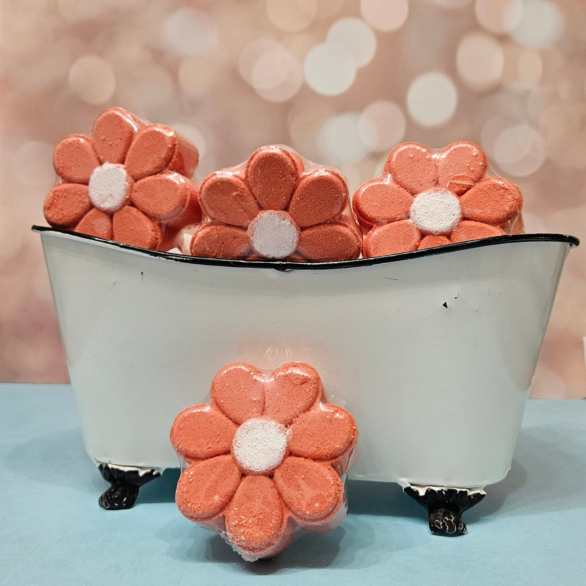 Flower-shaped bath bombs in a miniature white bathtub. Coral petals, white center. 