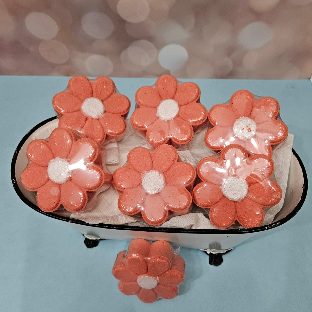 Flower-shaped coral bath bombs with white centers in a miniature bathtub.