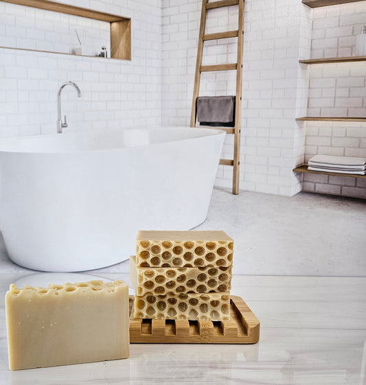 Handmade soap bars on a bamboo holder, one with honeycomb pattern. Bathroom background.