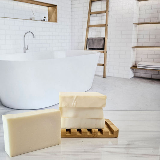 Handmade lavender castile soap bars, made with olive oil and lavender essential oil, on a wooden soap dish in a bathroom setting.