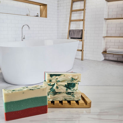 Handmade soap bars on a bamboo dish. One bar is layered red, green, and cream; others are swirled green and cream.