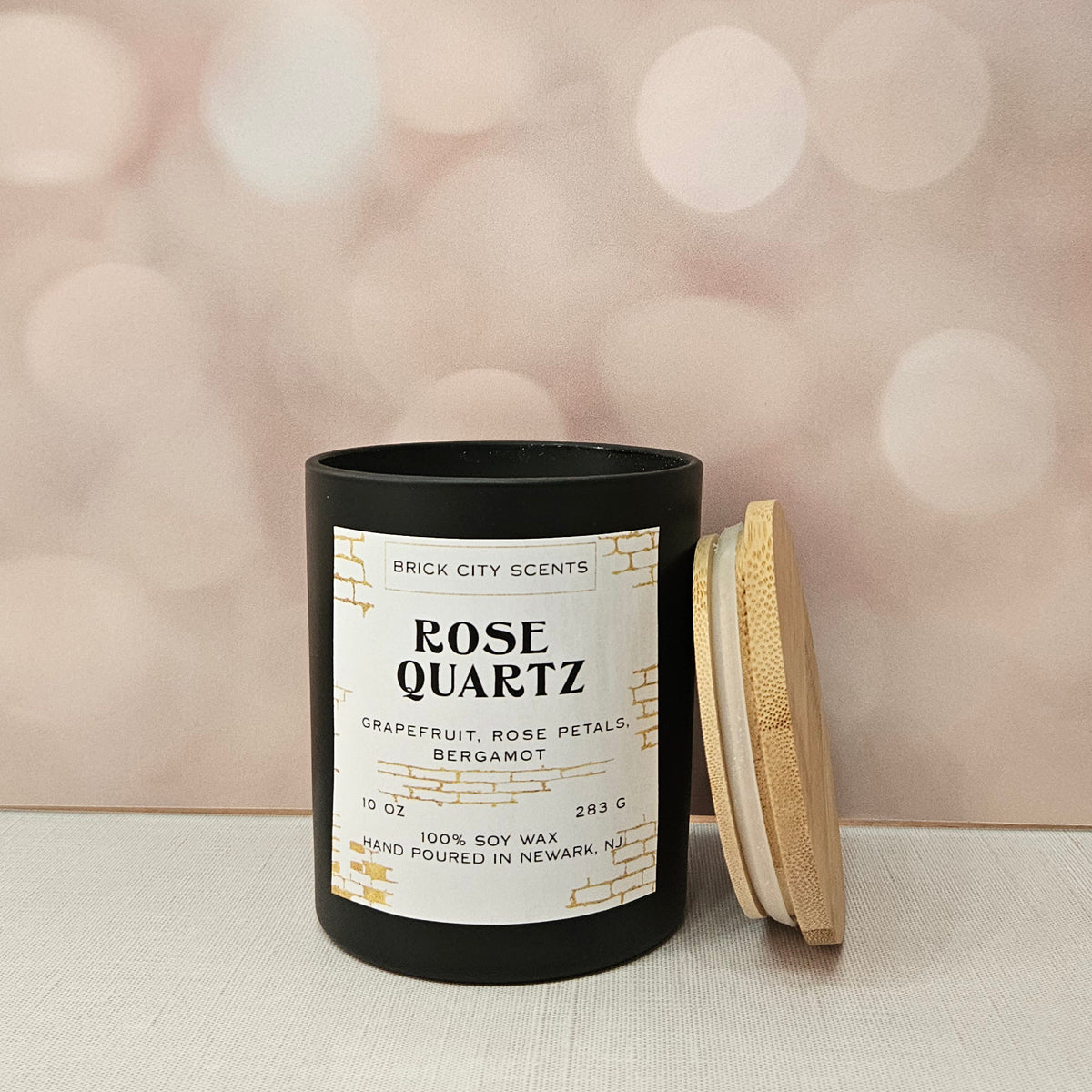 Brick City Scents Rose Quartz candle in a black jar with a wooden lid. Scent notes: grapefruit, rose petals, bergamot.