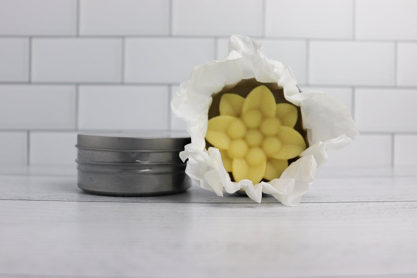 Flower-shaped lotion bar wrapped in paper, next to a metal tin container.